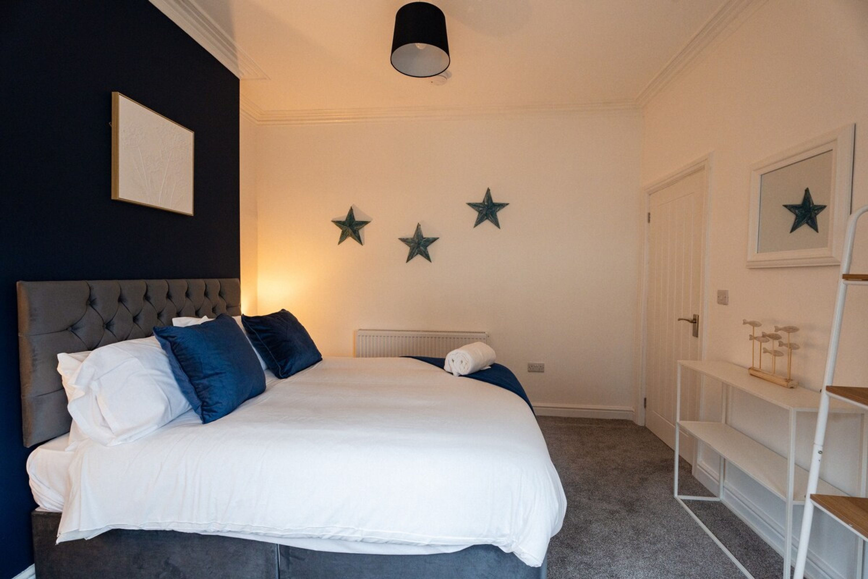 A bedroom with a large bed, a radiator, a shelf with decorative items, and a door.