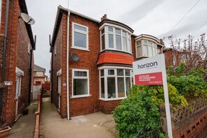 A two-story brick house with a satellite dish, a bay window, and a sign indicating it is managed by Horizon Property Group. - Buckingham House Horizon Stays (Redcar)