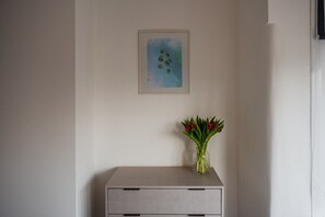 A room with a light-colored wall, a framed artwork, and a vase with red flowers on a small table. - Buckingham House Horizon Stays (Redcar)