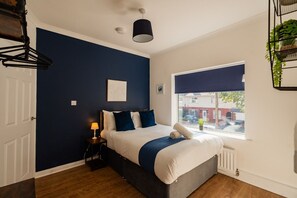 A bedroom with a bed, a bedside lamp, a window with a view, and a hanging plant. - Lime House Horizon Stays (Redcar)