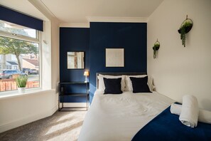 A hotel room with a bed, a nightstand, a lamp, a window with a view of the outside, and a wall-mounted plant. - Lime House Horizon Stays (Redcar)