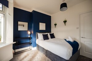 A bedroom with a bed, bedside table, lamp, wall-mounted plants, and a door. - Lime House Horizon Stays (Redcar)