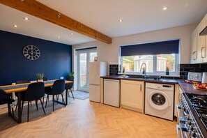 A modern kitchen with a dining area, wooden ceiling beams, and a view of the outside. - Lime House Horizon Stays (Redcar)