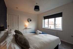 Une chambre à coucher avec un lit, une fenêtre donnant sur un paysage agréable, une porte et un luminaire fixé au mur.