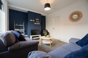 A modern living room with a sofa, a television, a small table, and decorative shelves. - Barnaby House Horizon Stays (Middlesbrough)