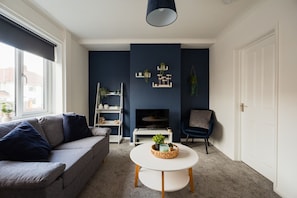 A modern living room with a grey sofa, a white coffee table, a TV, and a dark blue accent wall. - Barnaby House Horizon Stays (Middlesbrough)