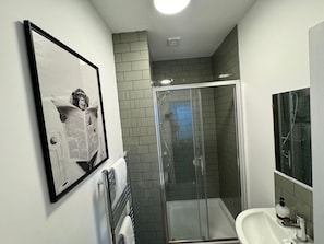 Ein Badezimmer mit Glasdusche, einem weißen Waschbecken und einem gerahmten Bild an der Wand.