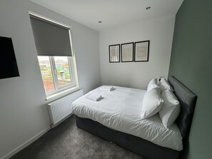 Ein Schlafzimmer mit einem Bett, einem Heizkörper, einem Fenster und drei gerahmten Bildern an der Wand.