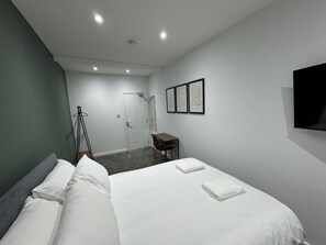 Ein Hotelzimmer mit einem Bett, einem Schreibtisch, einem Stuhl, einem Kleiderhaken und einem Fernseher.