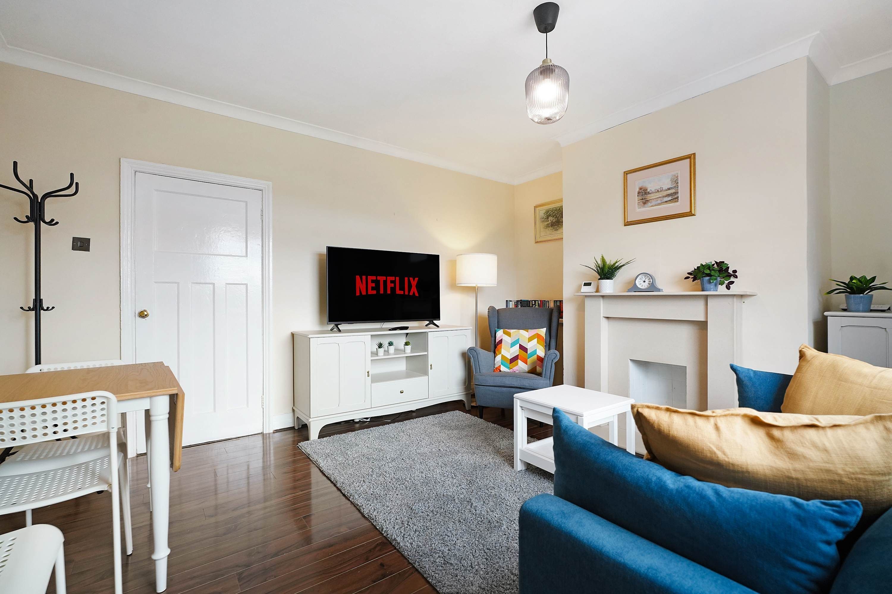 Una sala de estar con televisor de pantalla plana, sofá, mesa de centro, lámpara, perchero y chimenea.