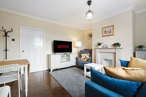 Ein Wohnzimmer mit Flachbildfernseher, einer Couch, einem Couchtisch, einer Lampe, einem Kleiderständer und einem Kamin.