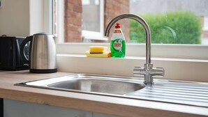 A kitchen sink with a faucet, a kettle, a bottle of Fairy dish soap, and a sponge on the counter. - Stunning 3BR Equipped Kitchen By Stay With Us (Chester-le-Street)