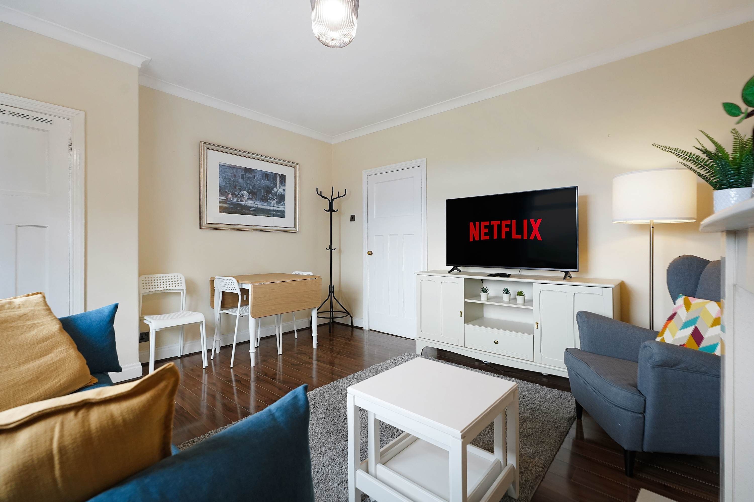 A living room with a flat-screen TV, a coat rack, a framed picture on the wall, and a sofa.