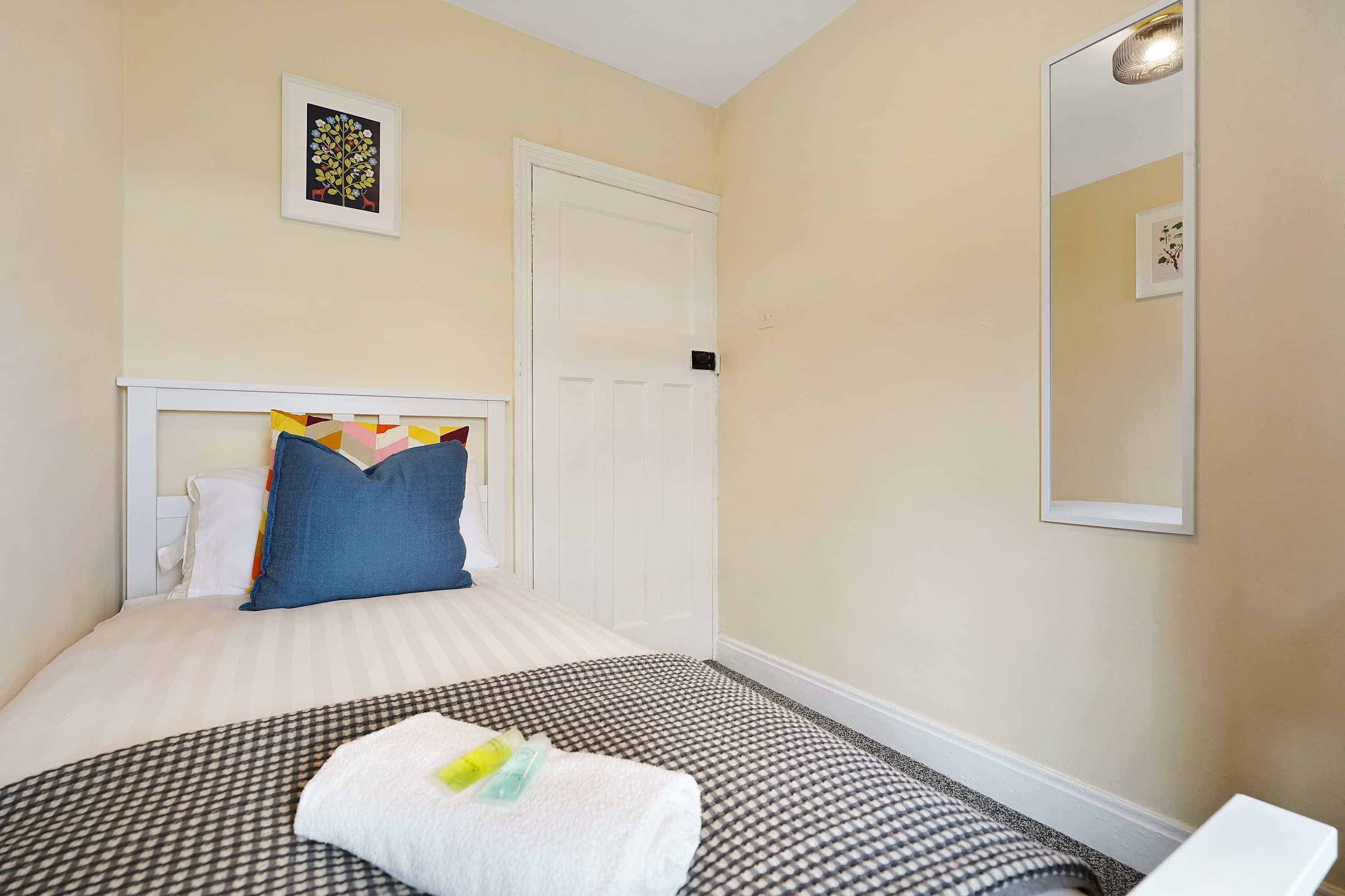 Un dormitorio con una cama, un almohadón, una mesita de noche, un espejo y una puerta.