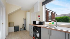 A compact kitchen with a washing machine, a sink, and a window overlooking a brick wall. - Stunning 3BR Equipped Kitchen By Stay With Us (Chester-le-Street)