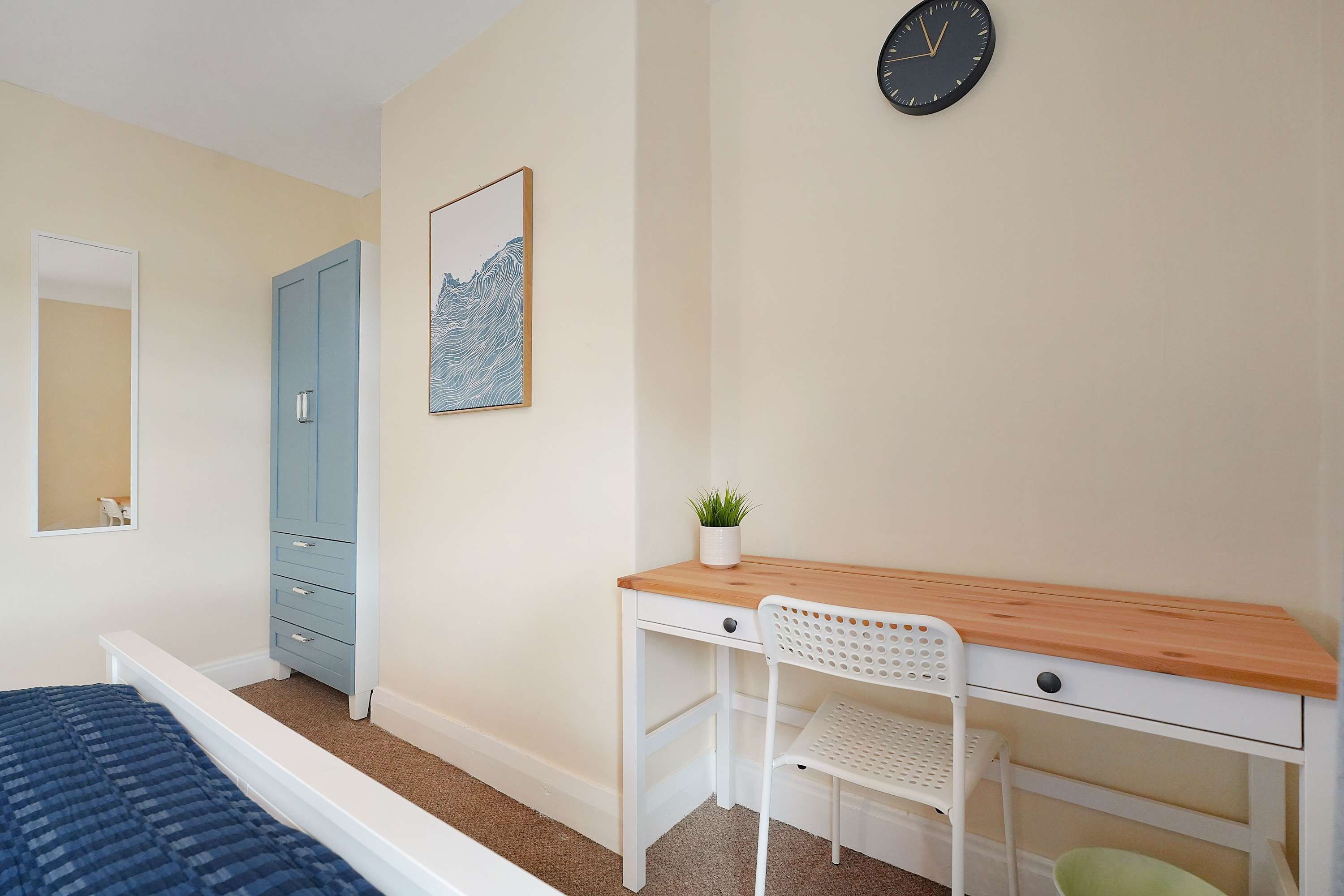 Une chambre à coucher comprenant un lit, un bureau avec une chaise, une armoire, un miroir, une horloge et une œuvre d’art accrochée au mur.