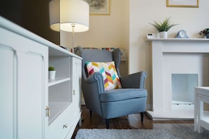 Ein Wohnzimmer mit grauem Sessel, weißem Kamin und Bücherregal.