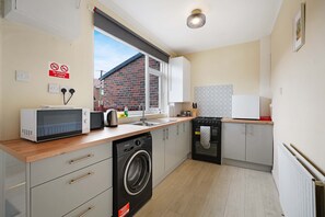 A compact kitchen with a microwave, toaster, sink, and washing machine. - Stunning 3BR Equipped Kitchen By Stay With Us (Chester-le-Street)
