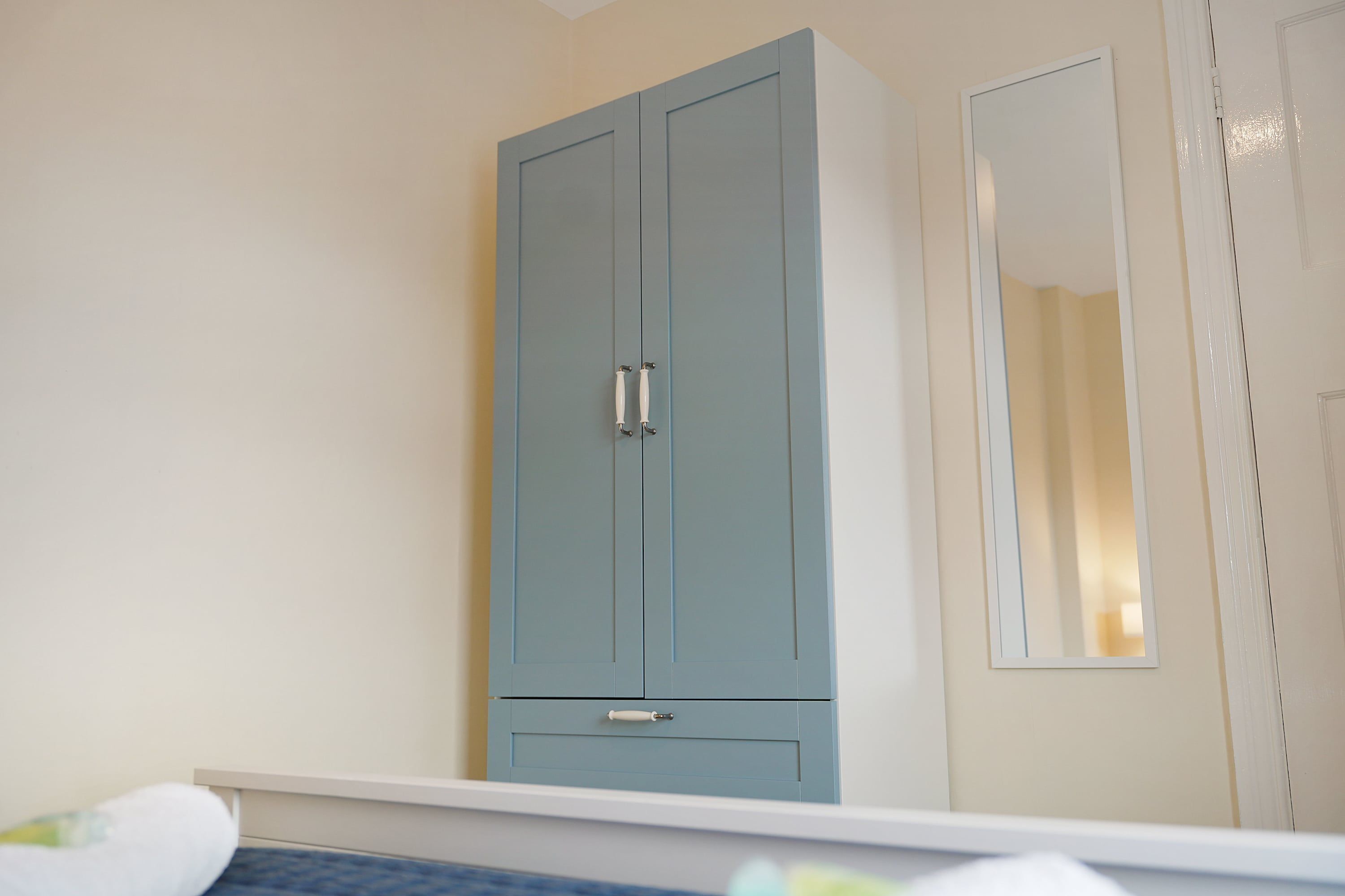 A bedroom with a light blue wardrobe, a white door, and a mirror on the wall.