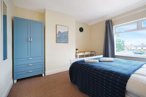 A bedroom with a bed, a wardrobe, a desk with a chair, a clock, and a window with curtains. - Stunning 3BR Equipped Kitchen By Stay With Us (Chester-le-Street)