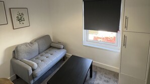 A room with a grey sofa, a black coffee table, a window with a blind, a ceiling light fixture, and a white cabinet. - Romney House Central Middlesbrough (Middlesbrough)