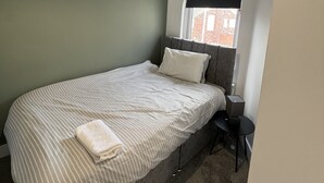 A bedroom with a bed, a bedside table, a lamp, and a window with a blind. - Romney House Central Middlesbrough (Middlesbrough)