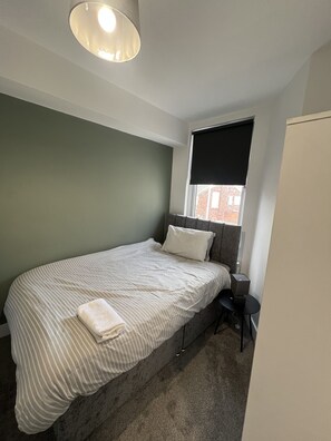 Ein Schlafzimmer mit einem Bett, einem Nachttisch, einer Lampe und einem Fenster mit Jalousie.