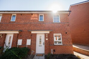 A red brick building with three doors and windows, a visible number '15' on the wall, and a small garden area with a welcome mat. - The Norton Nook Horizon Stays (Stockton-on-Tees)