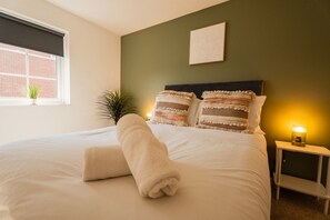 A neatly made bed with a rolled towel, a nightstand with a lamp, and a window with a view of a brick building. - The Norton Nook Horizon Stays (Stockton-on-Tees)