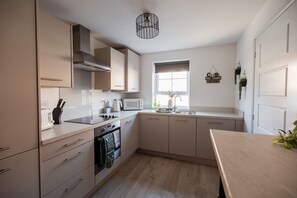 A modern kitchen with a built-in oven, microwave, and stove. There is a window with a view of the outside, and a hanging light fixture above the sink. - The Norton Nook Horizon Stays (Stockton-on-Tees)