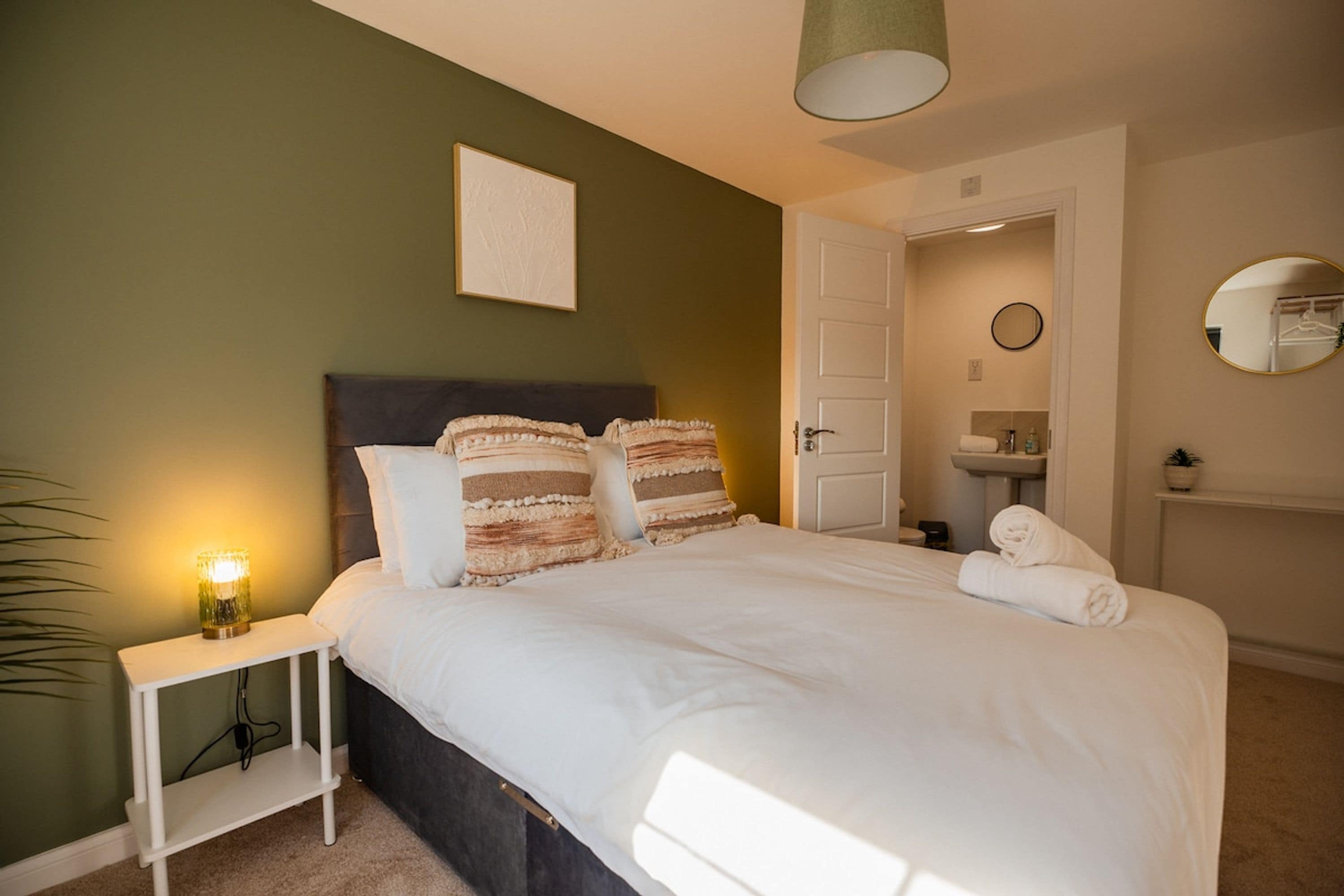 A neatly made bed with a headboard, a bedside lamp, and a wall-mounted mirror.