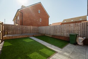 Un jardin avec une clôture en bois, une pelouse verdoyante et une maison en briques.
