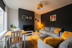 A modern living room with a sofa, a coffee table, a TV, and a dining area with a table and chairs. - Humber House Thornaby (Stockton-on-Tees)