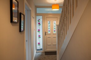 Un couloir avec un escalier menant à une porte dont les panneaux de verre dépoli présentent des motifs de roses.