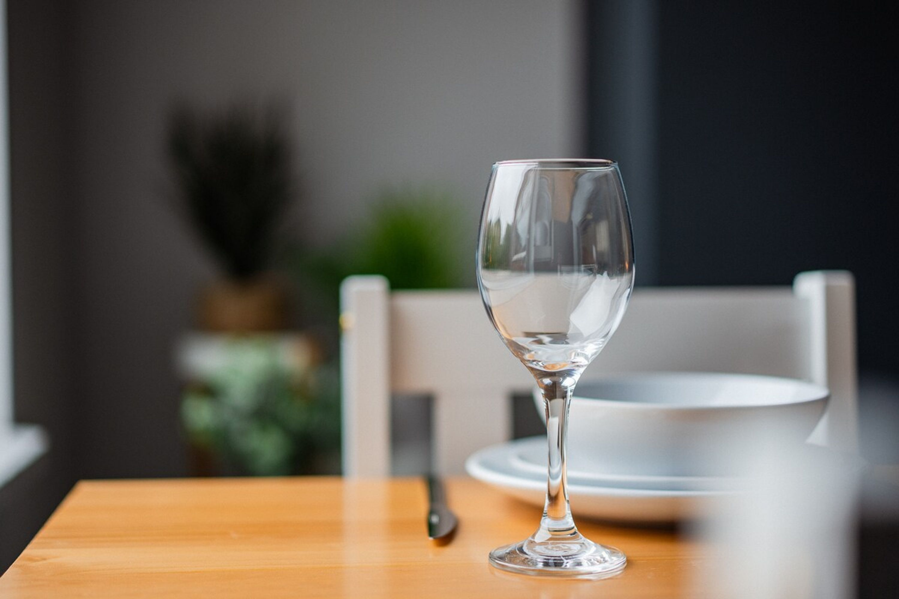 Una copa de vino de vidrio transparente sobre una mesa de madera, con un fondo desenfocado.