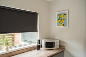 A kitchen with a microwave on the counter, a window with a dark roller blind, and a poster of lemons on the wall. - Humber House Thornaby (Stockton-on-Tees)