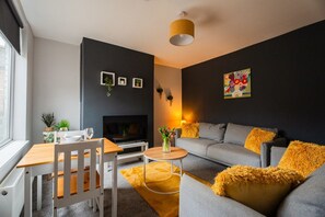 Un salon moderne avec un canapé gris, une table à manger en bois et un téléviseur.