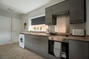 Eine moderne Küche mit grauen Schränken, einer integrierten Waschmaschine, einem Toaster und einem Fenster mit Blumentöpfen.