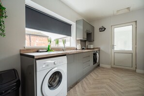 Une cuisine moderne équipée d’un lave-linge, d’une machine à café et d’une fenêtre donnant sur un immeuble en briques.