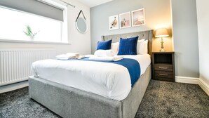 A neatly arranged hotel room with a bed, bedside table, lamp, and artwork on the wall. - Dalkeith House Horizon Stays 4 Bed (Hartlepool)