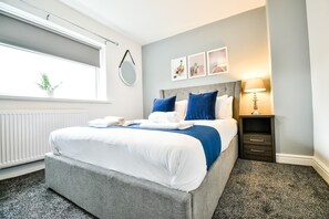 Ein ordentlich eingerichtetes Hotelzimmer mit Bett, Nachttisch, Lampe und einem Bild an der Wand.