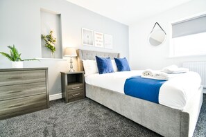 Ein Hotelzimmer mit einem Bett, einem Nachttisch, einer Kommode, einem Spiegel und einem Fenster.