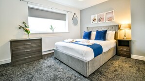 A bedroom with a bed, bedside tables, a radiator, a window with blinds, and wall-mounted pictures. - Dalkeith House Horizon Stays 4 Bed (Hartlepool)
