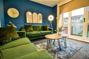 Ein Wohnzimmer mit einem grünen Sofa, einem runden Couchtisch und einer Stehlampe.