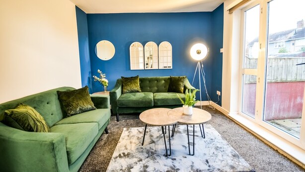 A living room with a blue wall, two green sofas, a round coffee table, and a floor lamp. - Dalkeith House Horizon Stays 4 Bed (Hartlepool)