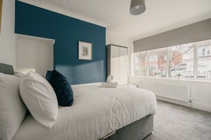 Un dormitorio con cama, ventana, radiador y un cuadro en la pared.