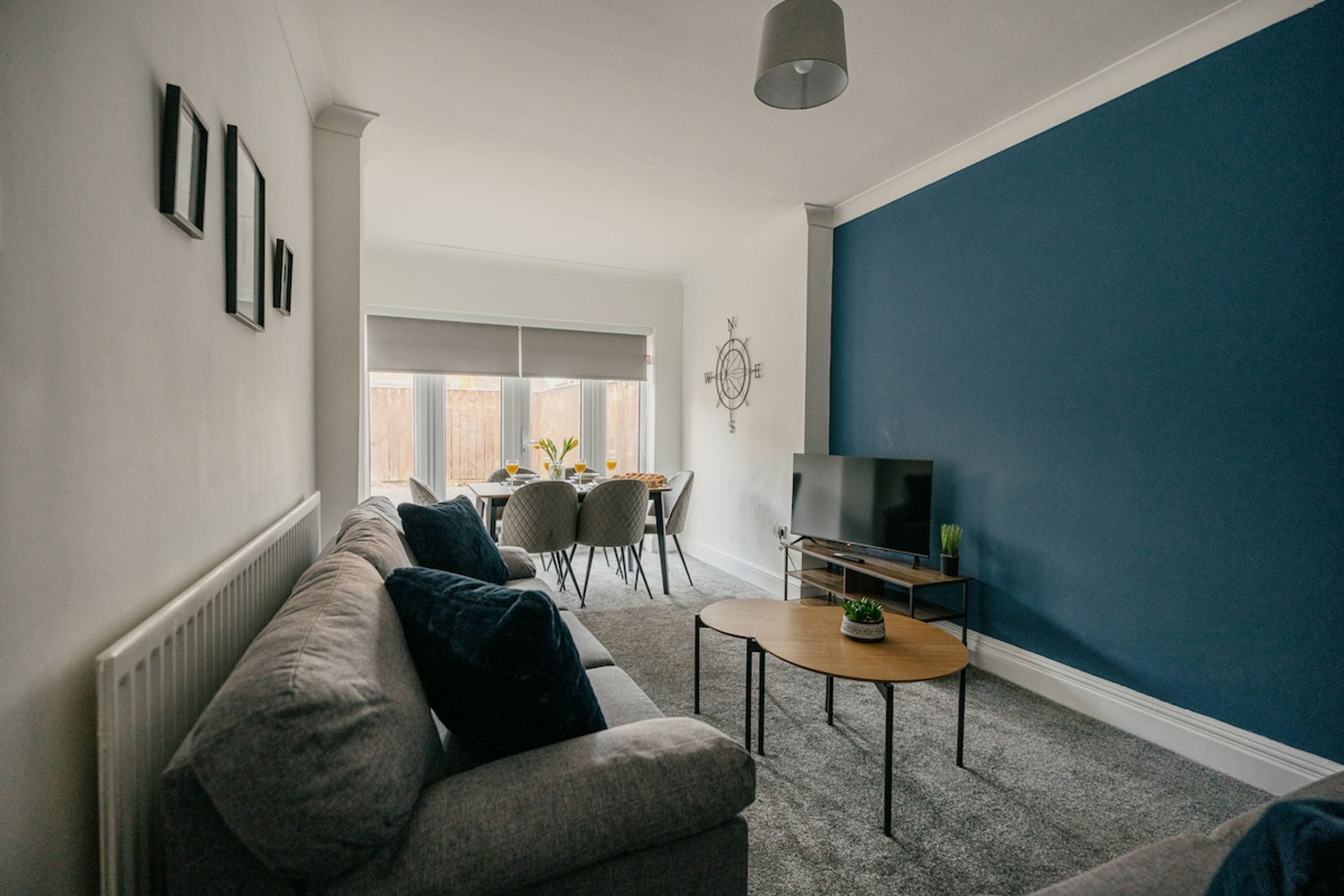 A modern living room with a grey sofa, a small round table, a TV, and a blue accent wall.