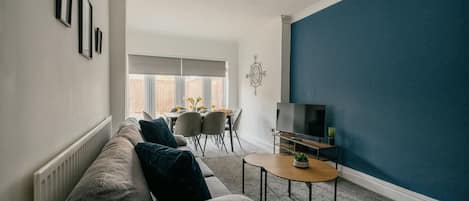 A modern living room with a grey sofa, a small round table, a TV, and a blue accent wall.