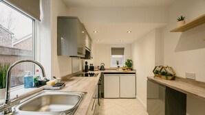 A modern kitchen with a built-in dishwasher, a window with a view of the outside, and a countertop with various items. - Canterbury House Horizonstays (Redcar)