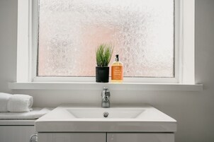 Un baño con un lavabo blanco, una ventana con vidrio esmerilado y una planta en maceta.